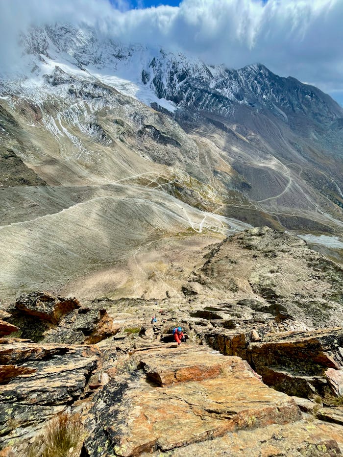 Scenic view of hikers ascending rocky mountain in Saas-Grund, Swiss Alps.