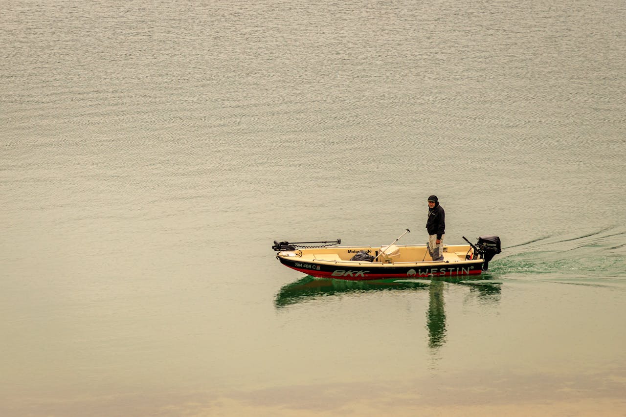 A lone man fishing on a calm lake in Serbia from a motorboat during the day.